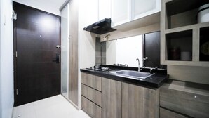 A modern kitchen with a black countertop, stainless steel sink, and wooden cabinets. - Homey Studio At Tamansari Papilio Apartment (Surabaya)