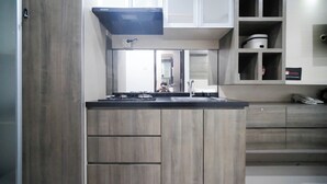 A modern kitchen with wooden cabinets, a built-in stove, and a microwave. - Homey Studio At Tamansari Papilio Apartment (Surabaya)