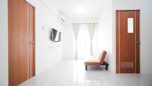 A hotel room with a wooden door, a television mounted on the wall, a bench, and a window with curtains.