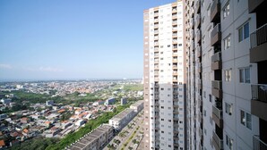 A high-rise building with multiple balconies and a view of a cityscape with various buildings and greenery.