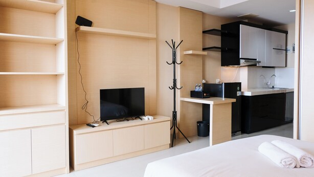 Ett modernt hotellrum med en säng, en TV, en klädställning, ett skrivbord med en dator och ett litet pentry.
