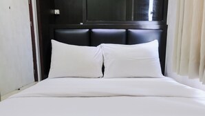 Una cama bien hecha con sábanas y almohadas blancas, un cabecero oscuro y una pared blanca con una puerta.
