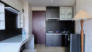 Una cocina compacta con microondas integrado, refrigerador y pileta. Hay una botella de agua sobre la encimera y una lámpara a la derecha.