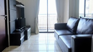 Una sala moderna con un sofá de cuero negro, un televisor de pantalla plana y un ventanal corredero a un balcón.