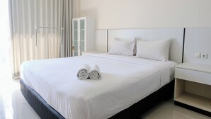 Hotelkamer met een groot bed, witte lakens, een nachtkastje en een glazen deur naar een balkon.