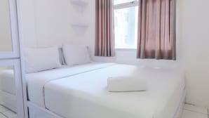 Un letto rifatto con lenzuola bianche e un cuscino, una finestra con tende e pareti bianche.