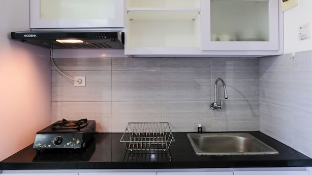 Una cucina con un piano di lavoro nero, un lavello in acciaio inox, un fornello a gas e pensili bianchi con vetri.