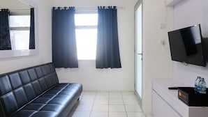 Una stanza con un divano in pelle nera, una televisione a schermo piatto su un mobile bianco e una finestra con tende nere.