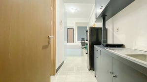 A narrow hallway with a kitchen area on the right, featuring a refrigerator, a microwave, and a sink. - Comfy And Modern Studio At Cordova Edupartment Semarang Apartment (Semarang)