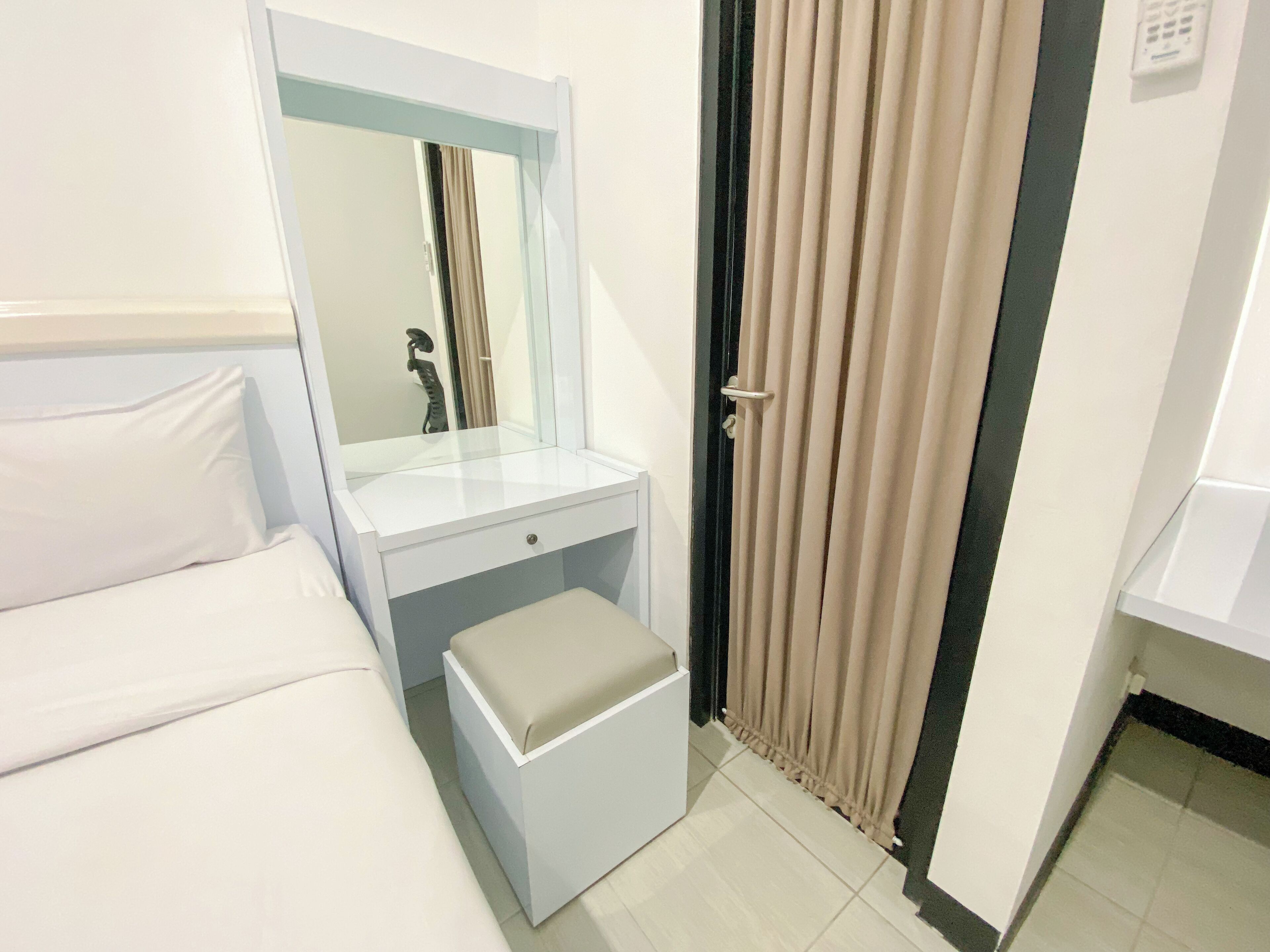 Camera d'albergo con un letto, un comodino, uno specchio, una porta del bagno e una tenda.