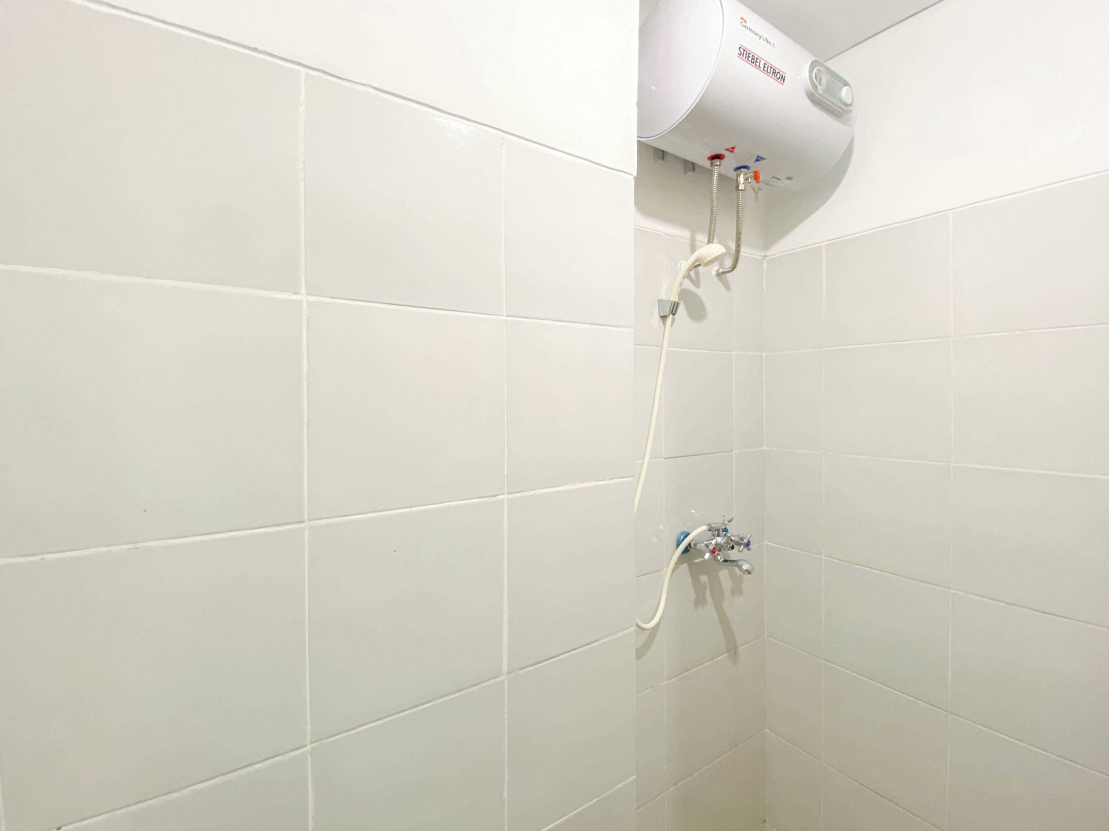 Zona de ducha con azulejos blancos, cabezal de ducha y panel de control.