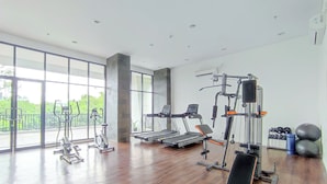 A spacious gym with cardio machines, free weights, and a bench. Large windows offer views of greenery outside. - Comfy And Modern Studio At Cordova Edupartment Semarang Apartment (Semarang)