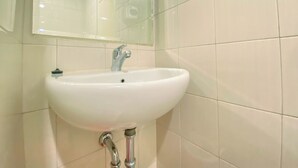 A bathroom with a white sink, a mirror, and tiled walls. - Minimalist Studio Apartment Signature Park Grande (Jakarta)
