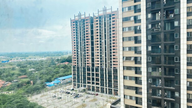 Un edificio de gran altura con varios pisos, un estacionamiento al frente y zonas verdes circundantes.