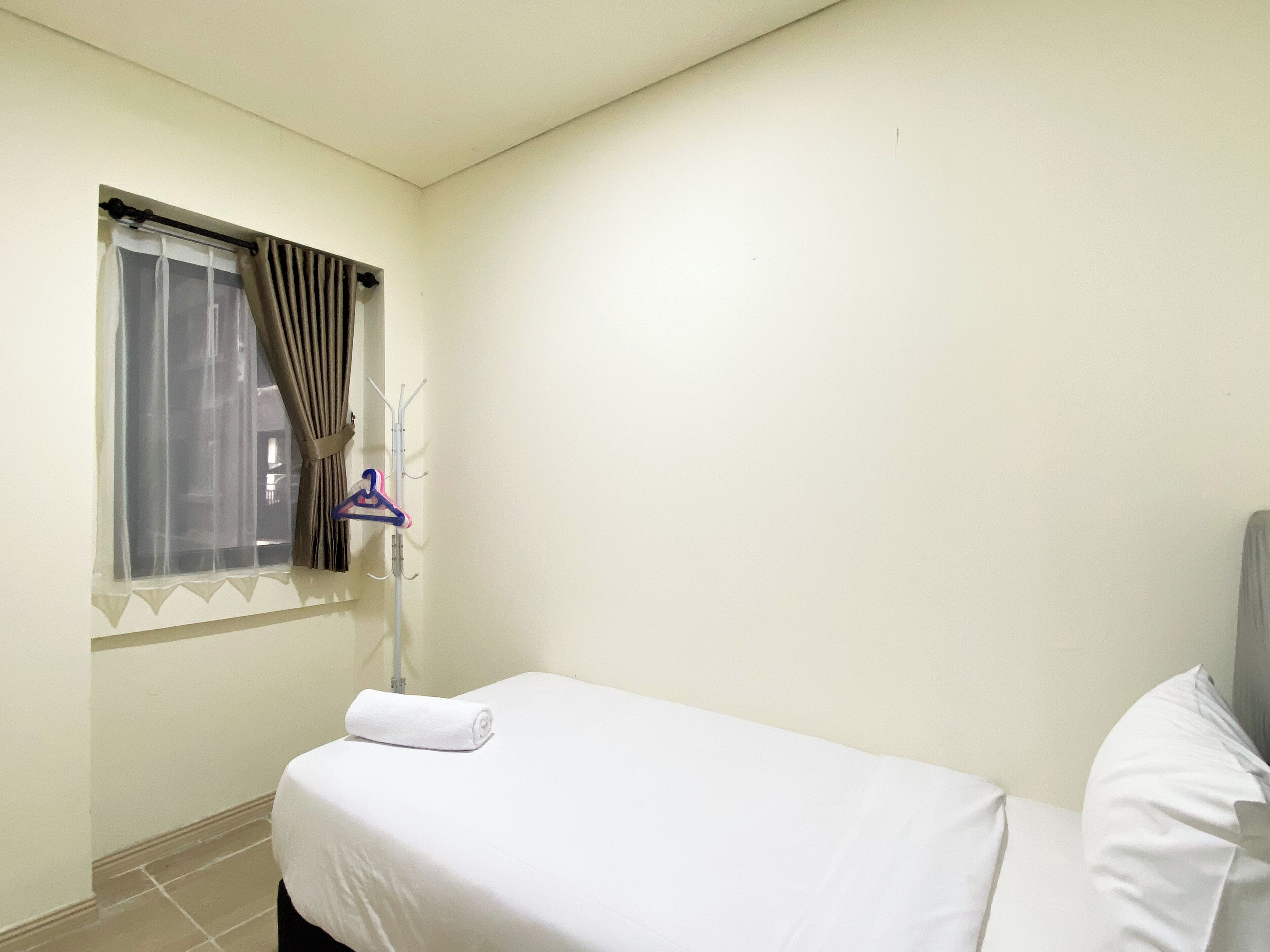 A small, simple room with a bed, a window with curtains, and a coat rack with a hanger.