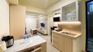 A modern kitchen with a marble countertop, a built-in microwave, and a sink. There is a dining area with a table and chairs, and a small seating area with a sofa. - Best Homey And Modern 2Br At Meikarta Apartment (Cikarang)