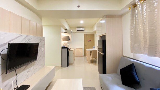 A modern living room with a flat-screen TV, a sofa, a coffee table, and a kitchen area in the background. - Best Homey And Modern 2Br At Meikarta Apartment (Cikarang)