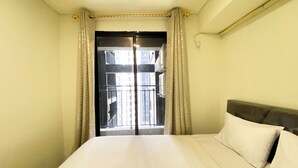 A hotel room with a bed, a bedside table, and a view of a building through a glass door. - Best Homey And Modern 2Br At Meikarta Apartment (Cikarang)