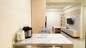 A modern hotel room with a marble dining table, two water bottles, a kettle, and a flat-screen TV mounted on a marble wall. - Best Homey And Modern 2Br At Meikarta Apartment (Cikarang)