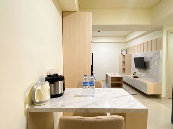 Habitación de hotel moderna con una mesa de comedor de mármol, dos botellas de agua, una tetera y un televisor de pantalla plana montado en una pared de mármol.