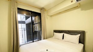 A hotel room with a bed, a window with curtains, and an air conditioning unit. - Best Homey And Modern 2Br At Meikarta Apartment (Cikarang)