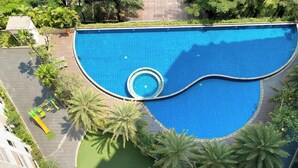 A large, uniquely shaped swimming pool surrounded by palm trees and greenery, with a small circular section in the center. - Spacious And Elegant Studio Apartment Mustika Golf Residence (Cikarang)