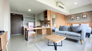 A modern living room with a sofa, a coffee table, and a kitchen area with a fridge and a sink. - Spacious And Elegant Studio Apartment Mustika Golf Residence (Cikarang)