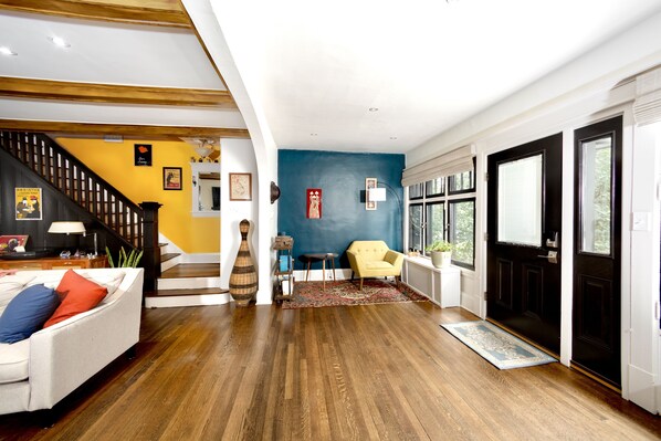 A spacious living room with hardwood flooring, a staircase, a yellow armchair, and a blue accent wall.