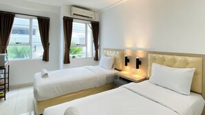 A hotel room with two beds, a bedside table with a lamp, an air conditioning unit, and a window with curtains. - Cozy Stay Studio (No Kitchen) Elvis Tower Apartment (Cikarang)