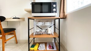 A kitchen area with a microwave on a shelf, a chair, and a window with curtains. - Cozy Stay Studio (No Kitchen) Elvis Tower Apartment (Cikarang)