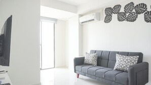 A modern living room with a grey sofa, two patterned cushions, a flat-screen TV, and an air conditioning unit on the wall. - Comfort Stay 2Br At Daan Mogot City Apartment (Jakarta)