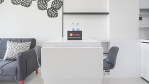 A modern, minimalist room with a grey sofa, a white table with a 'Travelio' sign, and a water dispenser. - Comfort Stay 2Br At Daan Mogot City Apartment (Jakarta)