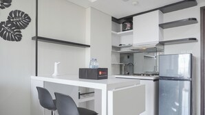 A modern kitchen with white cabinetry, a stainless steel refrigerator, and two black bar stools. - Comfort Stay 2Br At Daan Mogot City Apartment (Jakarta)