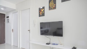A modern living room with a flat-screen TV mounted on the wall, a white entertainment unit below, and a door to the left. - Comfort Stay 2Br At Daan Mogot City Apartment (Jakarta)