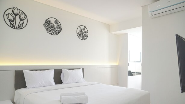 A modern hotel room with a large bed, white bedding, and three wall-mounted floral decorations. - Comfort Stay 2Br At Daan Mogot City Apartment (Jakarta)