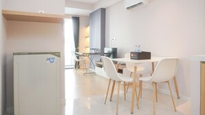A modern kitchen with white cabinets, a refrigerator, and a dining area with white chairs and a table. - Brand New And Comfy Studio At Daan Mogot City Apartment (Jakarta)