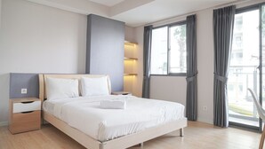 A modern hotel room with a wooden bed, a nightstand, a drawer, and a large window with curtains. - Brand New And Comfy Studio At Daan Mogot City Apartment (Jakarta)