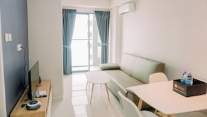 A modern hotel room with a sofa, a small table, a TV, and a desk with a computer and mouse.
