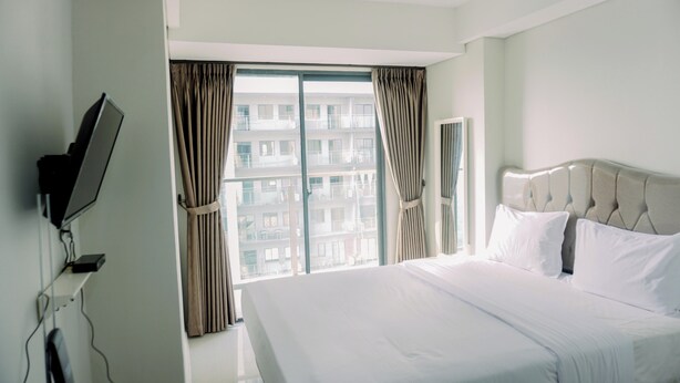 A hotel room with a large bed, a television mounted on the wall, and a window with curtains. - Pleasurable And Tidy Studio Daan Mogot City Apartment (Jakarta)