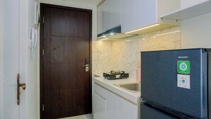A compact kitchen with a dark wooden door, white cabinets, a black refrigerator, and a marble backsplash. - Pleasurable And Tidy Studio Daan Mogot City Apartment (Jakarta)