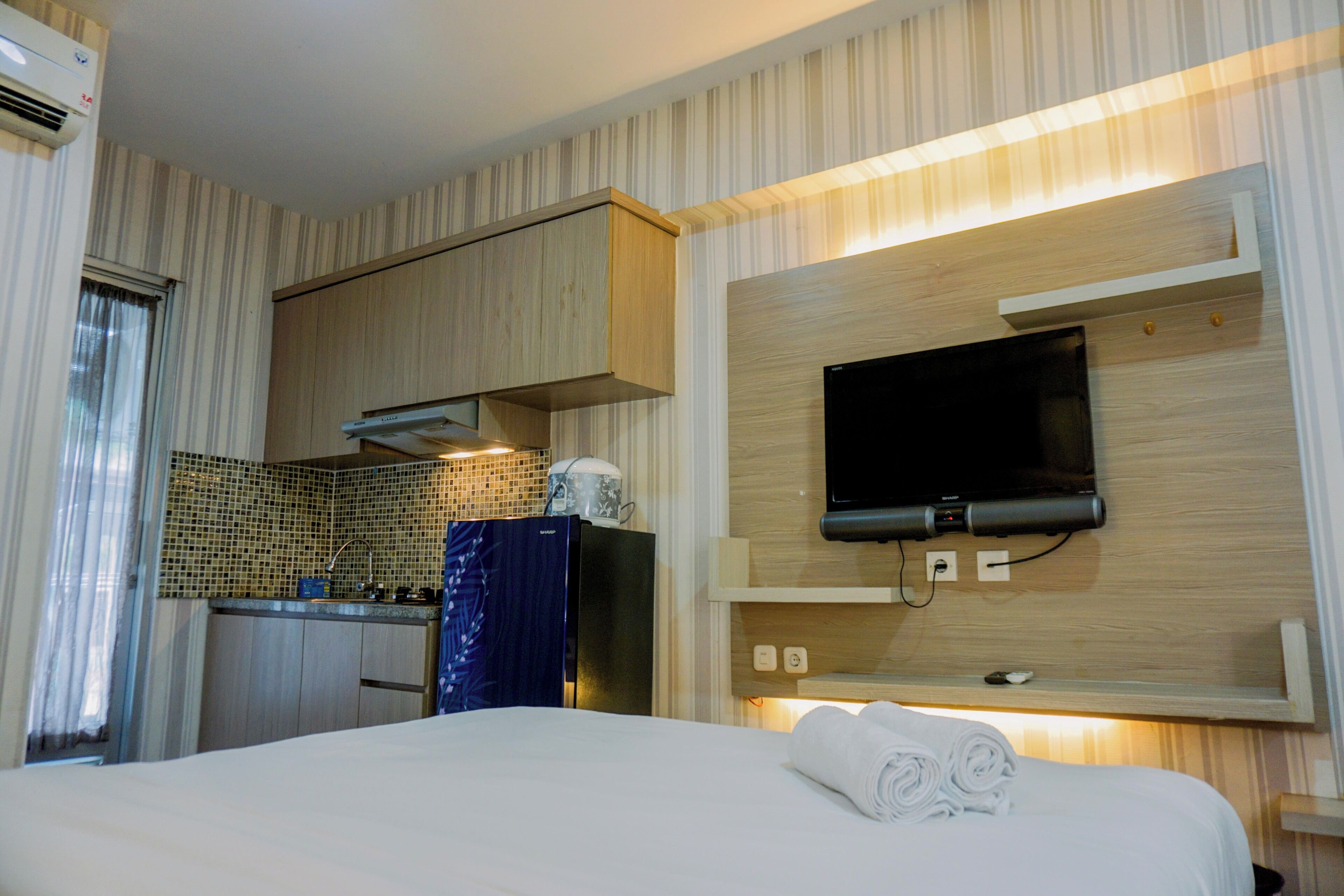 Quarto de hotel com cama, televisão fixada na parede, cozinha compacta e janela com cortinas.