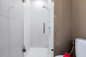 Un baño moderno con ducha de vidrio, azulejos blancos y un inodoro a la vista.