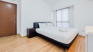 A bedroom with a bed, a nightstand, a wooden floor, a window with curtains, and an air conditioning unit.