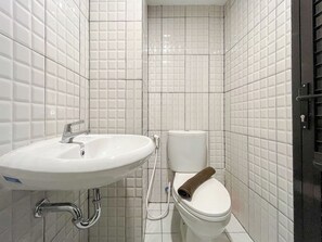 A bathroom with white tiled walls, a white sink with a chrome faucet, and a toilet with a towel on the lid.