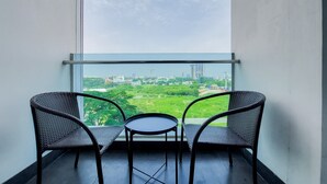 A balcony with two wicker chairs and a small table, overlooking a green park and cityscape.