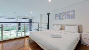 A modern bedroom with a large bed, a balcony with a railing, and a city view.