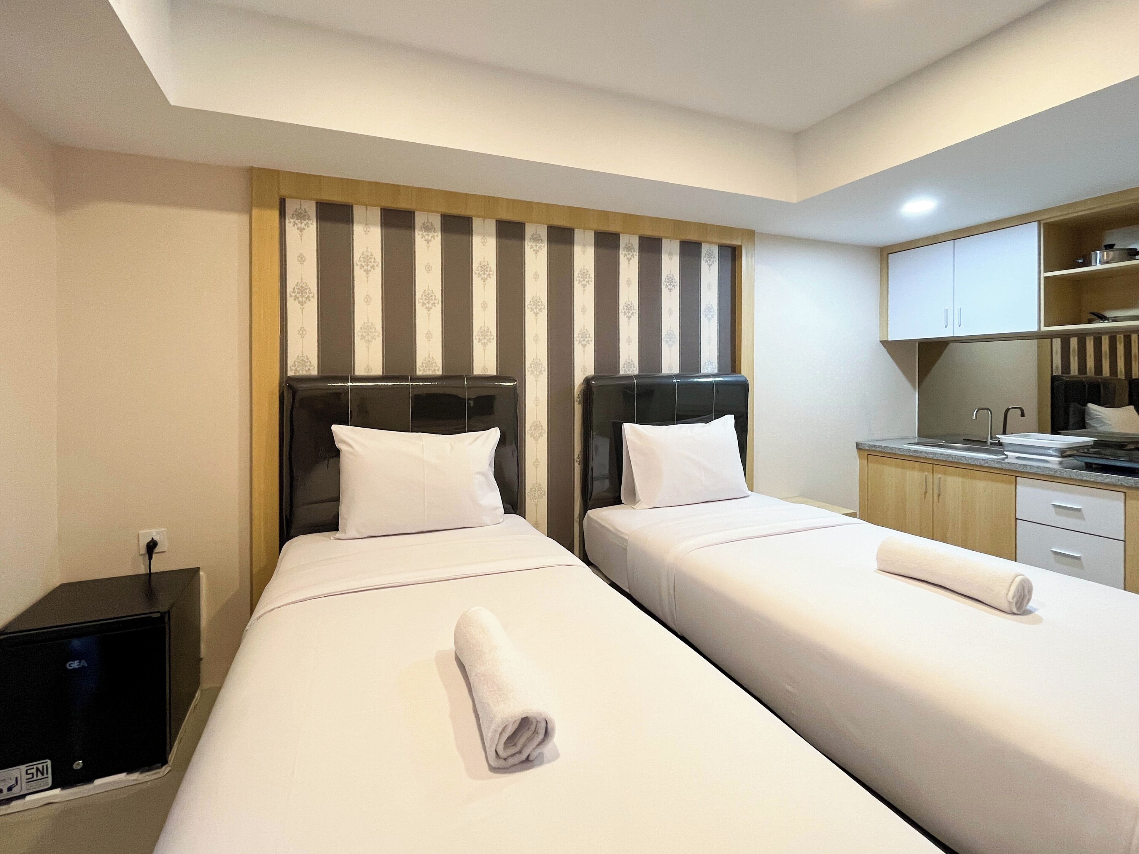 Quarto de hotel com duas camas, uma secretária pequena e uma cozinha compacta.
