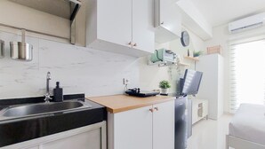 Cocina compacta con lavamanos, armarios, una encimera, refrigerador y televisor.