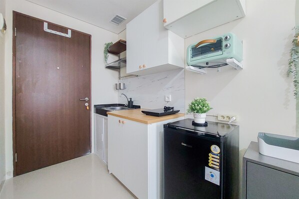 Cozinha compacta com armários brancos, geladeira preta, micro-ondas e um pequeno balcão.