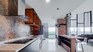 A modern kitchen with a marble countertop, wooden cabinets, and a brick accent wall. - Spacious 2Br Loft At Brooklyn Alam Sutera Apartment (South Tangerang)